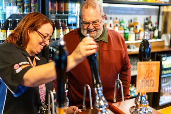 Member of bar staff showing a person how to pull a pint