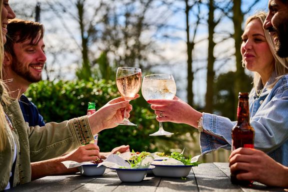 Four people sitting at an outdoor table, two of them raising their glasses to toast