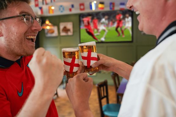 Two fans watching football match on a big screen with their limited edition pint glasses clinking