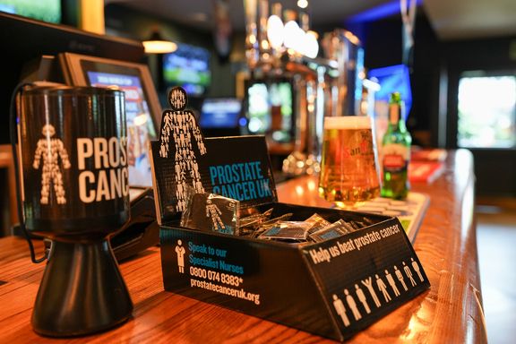 Prostate Cancer UK pin badge display and donation collection box on a pub bar
