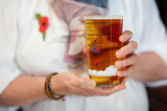Jane Wilkes in background holding commemorative pint glass in palm