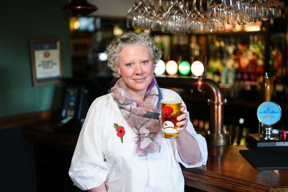 Jane Wilkes holding commemorative pint glass with bar scene in background