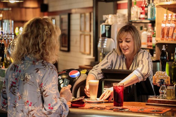 A pub team member serving a coffee to a customer at the bar