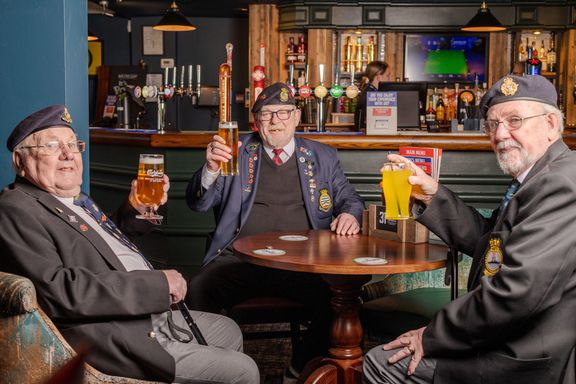 Three veterans sitting around a pub table raising their glasses